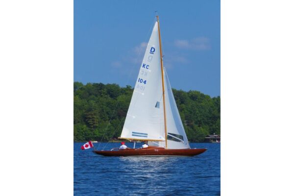 Vintage 1957 Dragon 29 sailboat on a lake with Canadian flag, clear blue sky.
