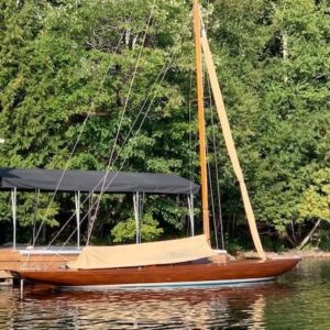 1957 Dragon 29 sailboat docked by a boathouse, surrounded by lush greenery.