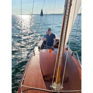 Man sailing on vintage 1957 Dragon 29 yacht, sunlit sea in background.